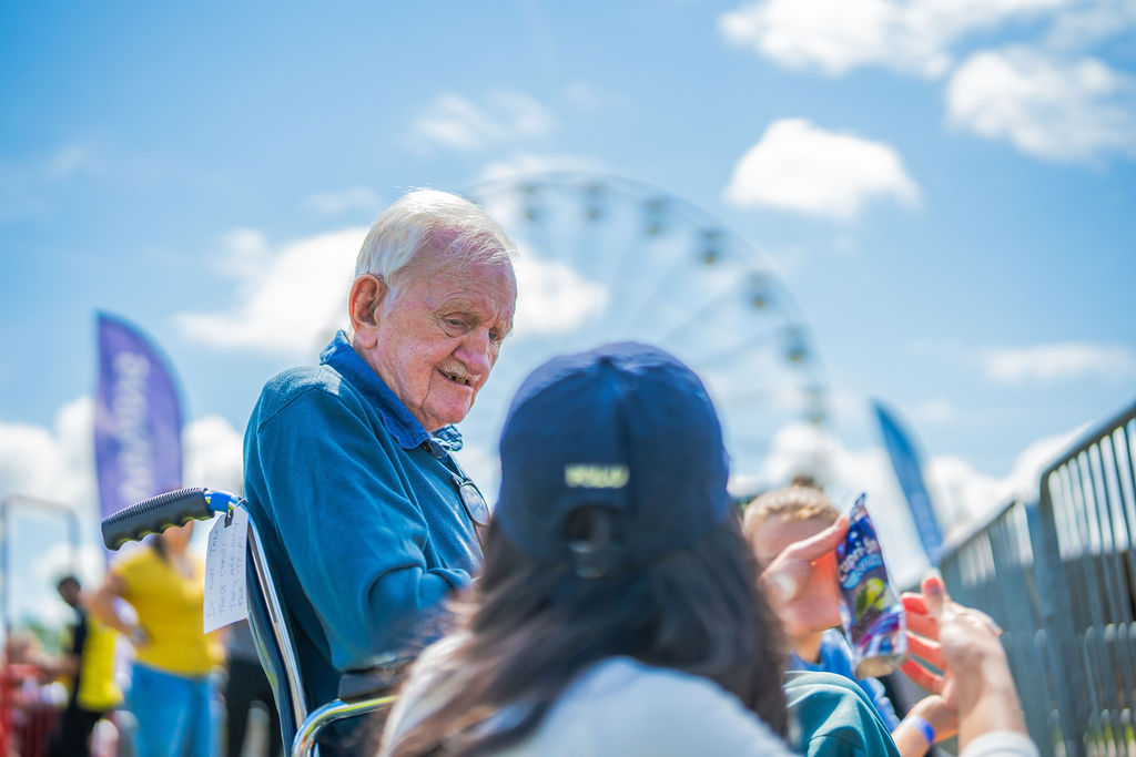 A resident and carer sit in front of a ferris wheel at a local balloon fiesta.