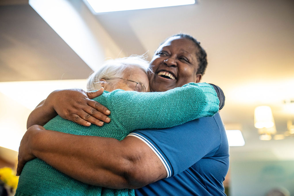 A resident and carer embrace in a hug.