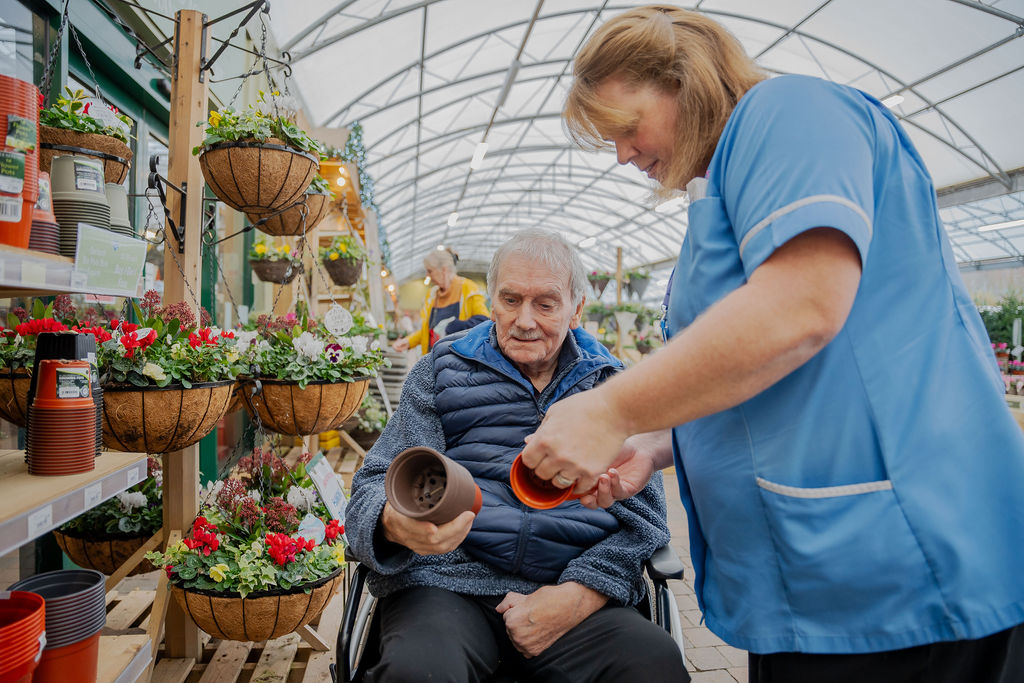 A male home care client and carer looking at plants at the garden centre.